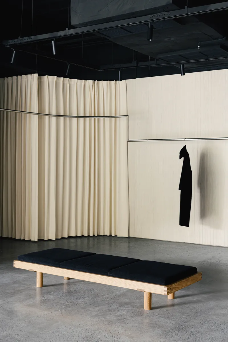 Fitting room area with curved fabric curtains and timber bench beneath exposed black ceiling
