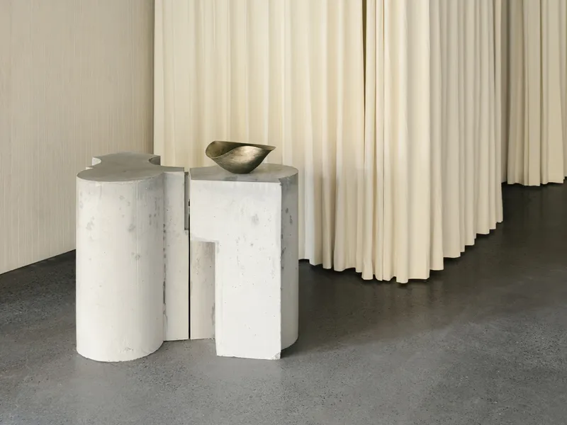 White concrete pedestals with sculptural bowl against pleated fabric panels and polished floor