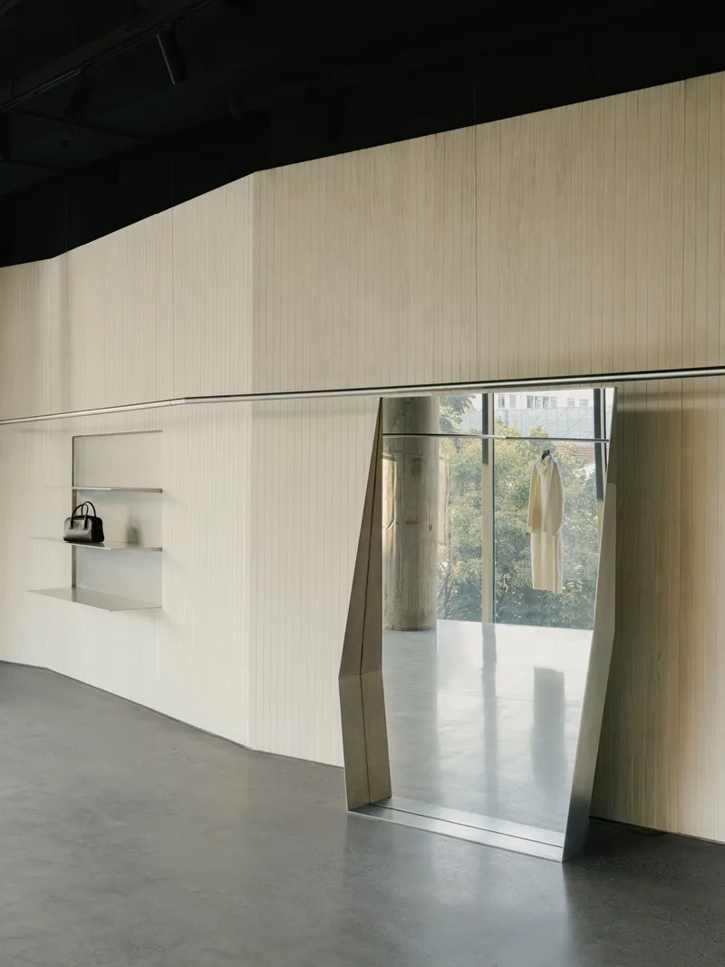 Angled doorway cut through ribbed wall with metal surround leading to daylit space beyond