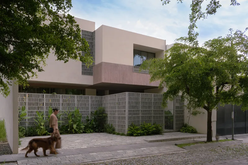 Street view of the perforated concrete screen wall beneath overhanging volumes with a person walking a dog