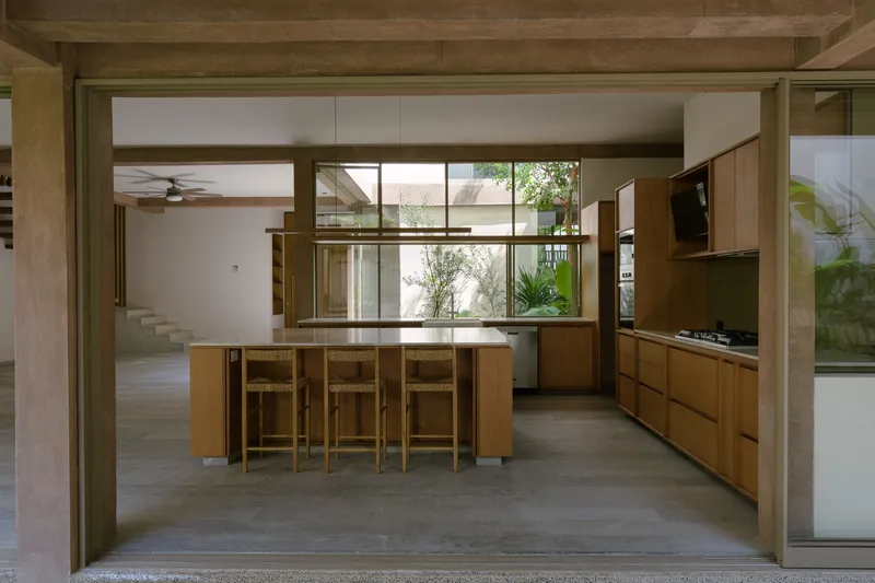 Open kitchen with timber island and stools framed by exposed timber beams and courtyard views