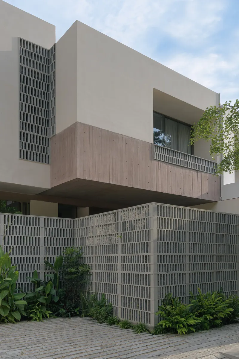 Street facade with cantilevered concrete volume above a perforated block wall and tropical landscaping