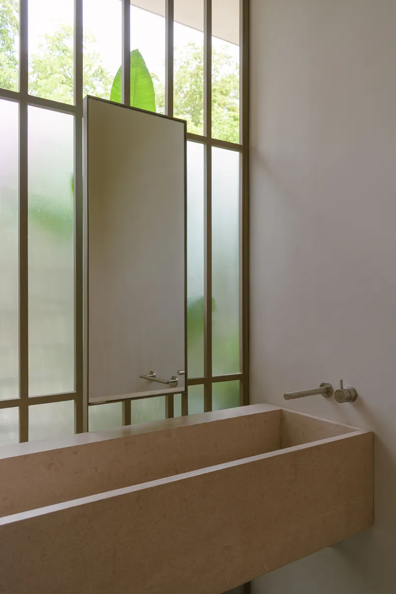 Bathroom with stone sink and steel-framed translucent glass partition revealing green foliage beyond