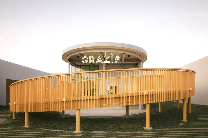 Circular pavilion with vertical timber slat screen and glass dome at dusk