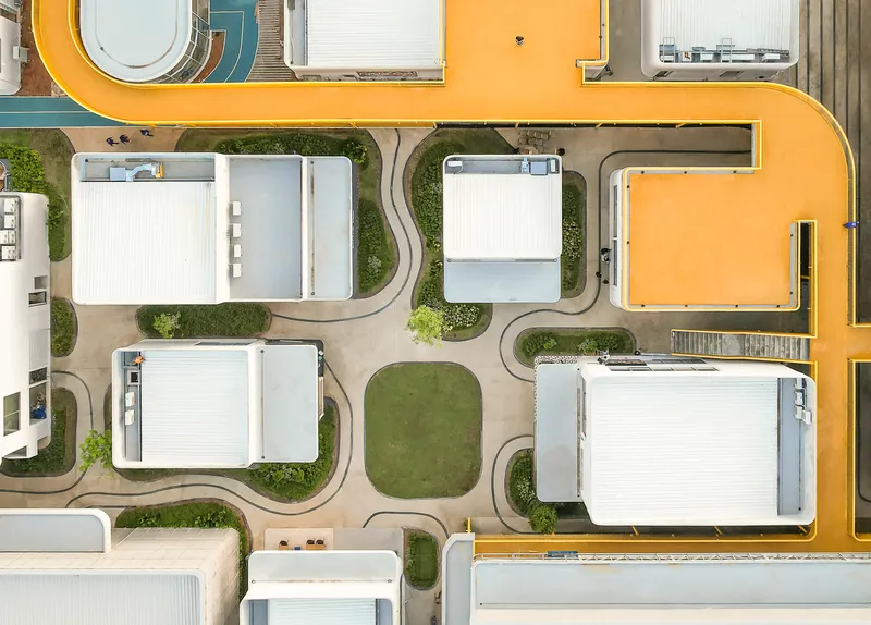Drone view of circulation paths threading through white roofed volumes and planted islands