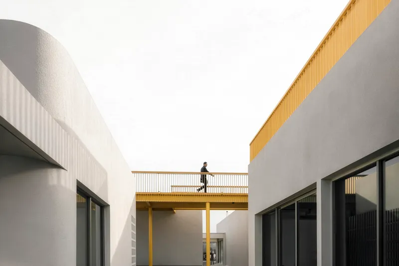 Elevated bridge with yellow railing connecting two white volumes with person crossing
