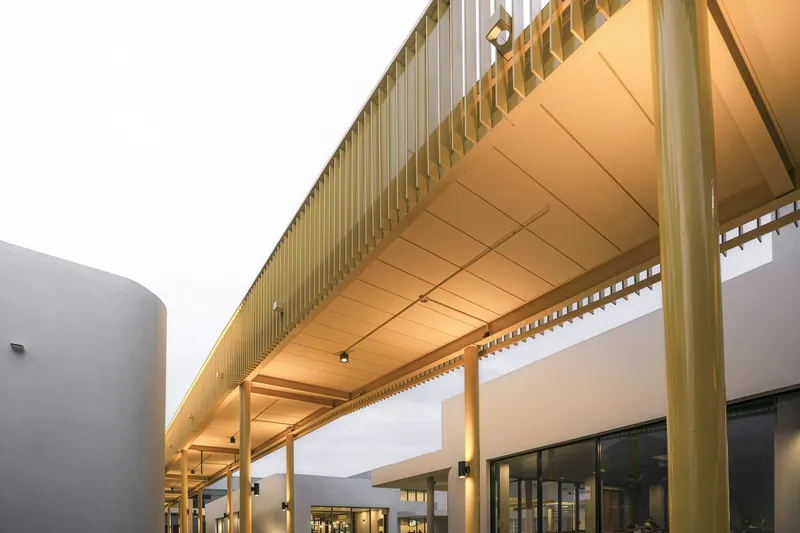 Covered walkway with timber slat canopy and illuminated wood ceiling at dusk
