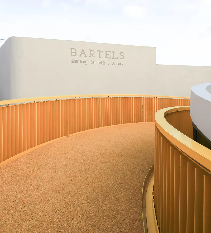 Curving service counter with vertical timber battens and cork flooring beneath signage wall