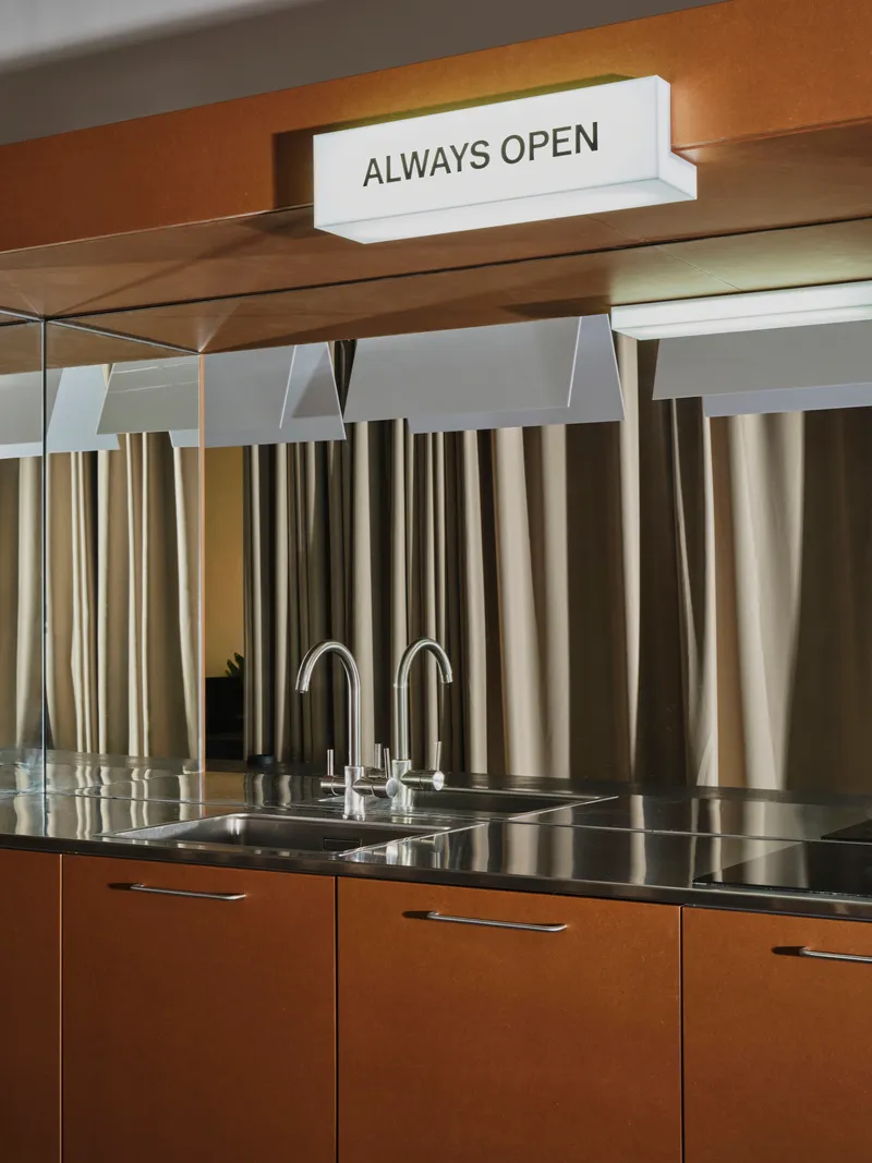 Kitchen counter with stainless steel sink and backsplash of vertical metal tubes beneath timber shelving