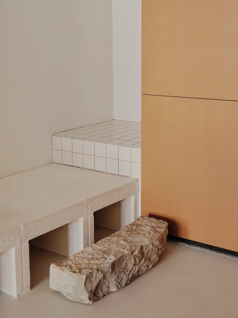 Corner detail showing white tiled bench with raw stone blocks on pale flooring beside timber panels