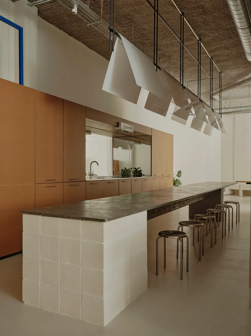 Island table with white concrete block base and timber cabinetry beyond in a space with exposed ductwork
