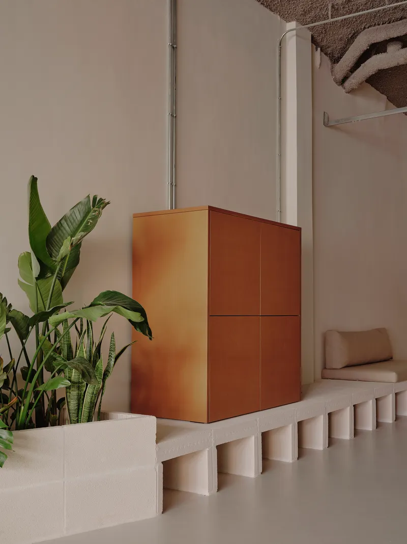 Copper-clad cubic volume on a fluted concrete plinth beside tropical plants and a white column