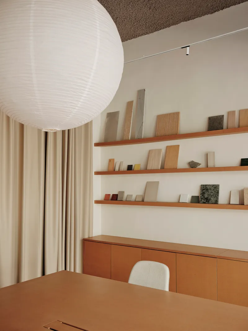 Timber shelving with material samples above a low cabinet and table beneath a spherical paper lantern