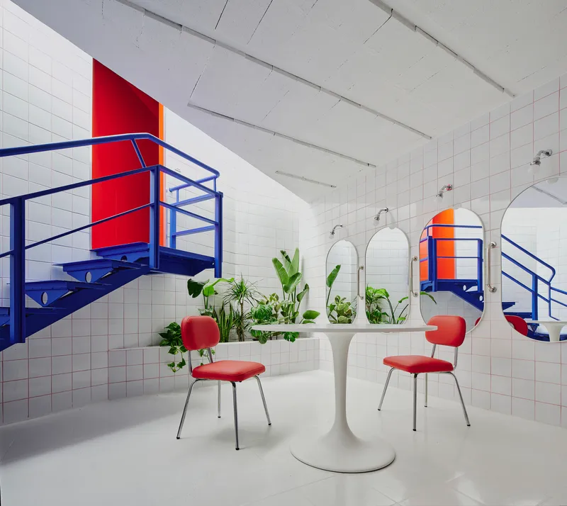 White tiled room with blue steel staircases, red accent panels, round mirrors and potted greenery