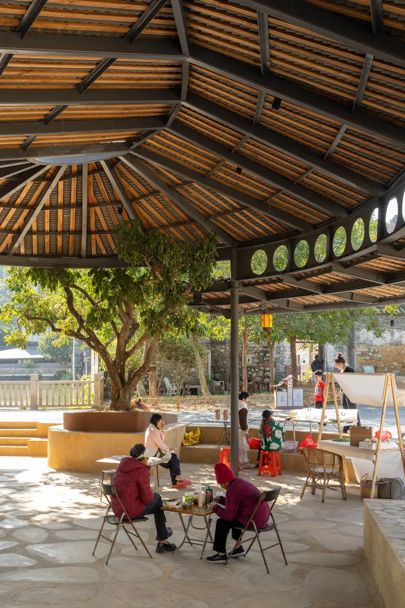 Interior courtyard with latticed timber roof, circular tree planter, and residents seated at tables below