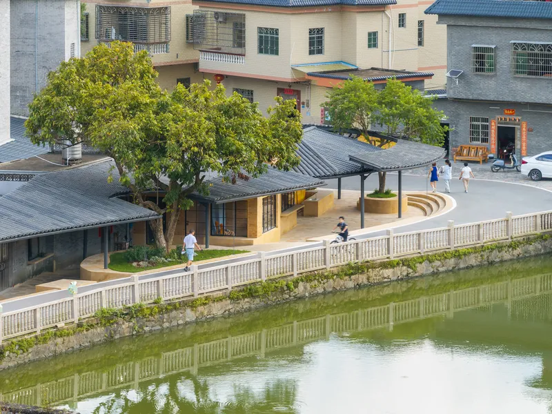 Curved tile roofs along a pond with white balustrade and pedestrians crossing the paved plaza