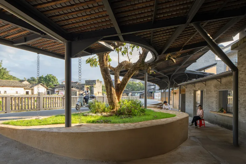 Covered walkway with exposed timber ceiling, steel columns, and a curved planter bed with tree