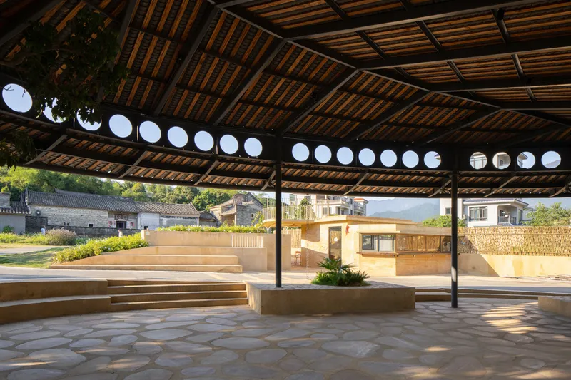 Covered pavilion with timber slat ceiling, steel columns and circular roof openings framing afternoon light