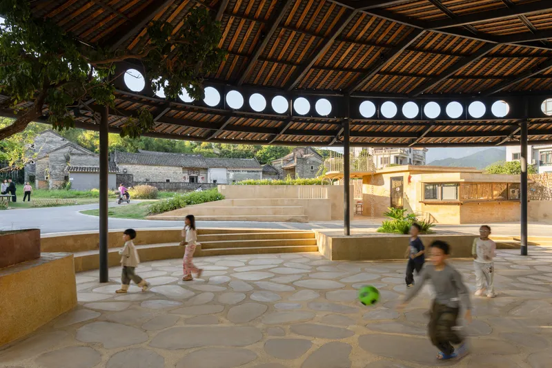 Pavilion interior with timber ceiling and circular openings framing children playing and a raised timber platform in the distance