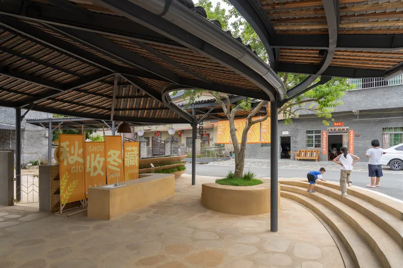 Curved timber steps with integrated planters beneath a pavilion roof with steel columns and bamboo ceiling structure
