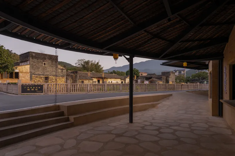 Stone-paved platform under timber ceiling with steel columns overlooking mountains in evening light