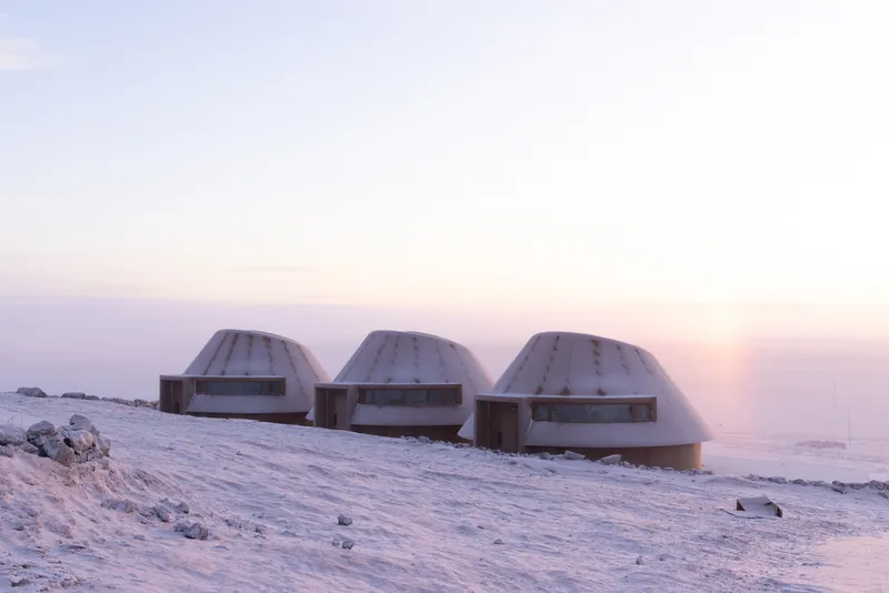 Three domed structures with horizontal ribbon windows set against a snowy hillside at sunset