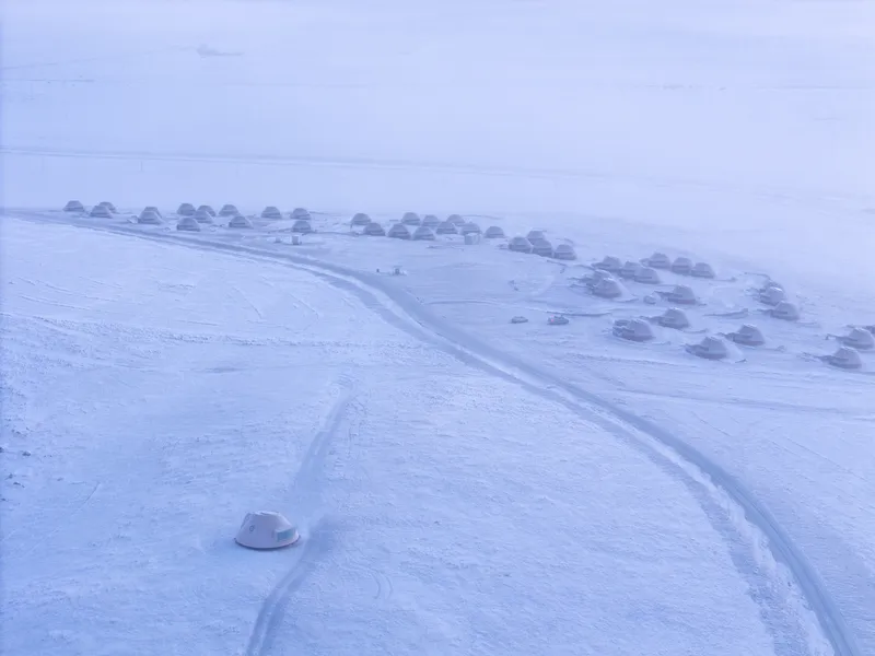 Aerial view of dome-roofed structures connected by curving pathways through a snow-covered settlement in twilight