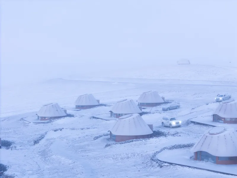 Cluster of conical-roofed structures with timber cladding and stone bases in heavy snowfall at dusk
