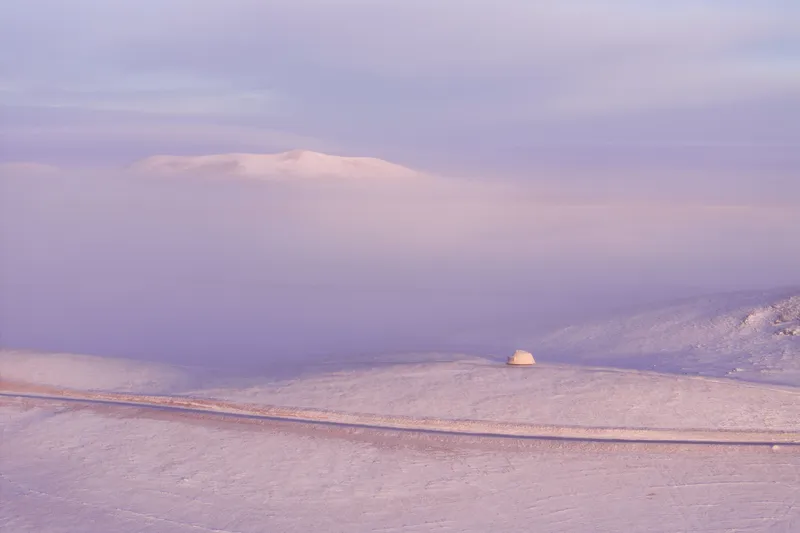 Dome shelter set in snowy valley with rolling hills and low cloud cover at dusk