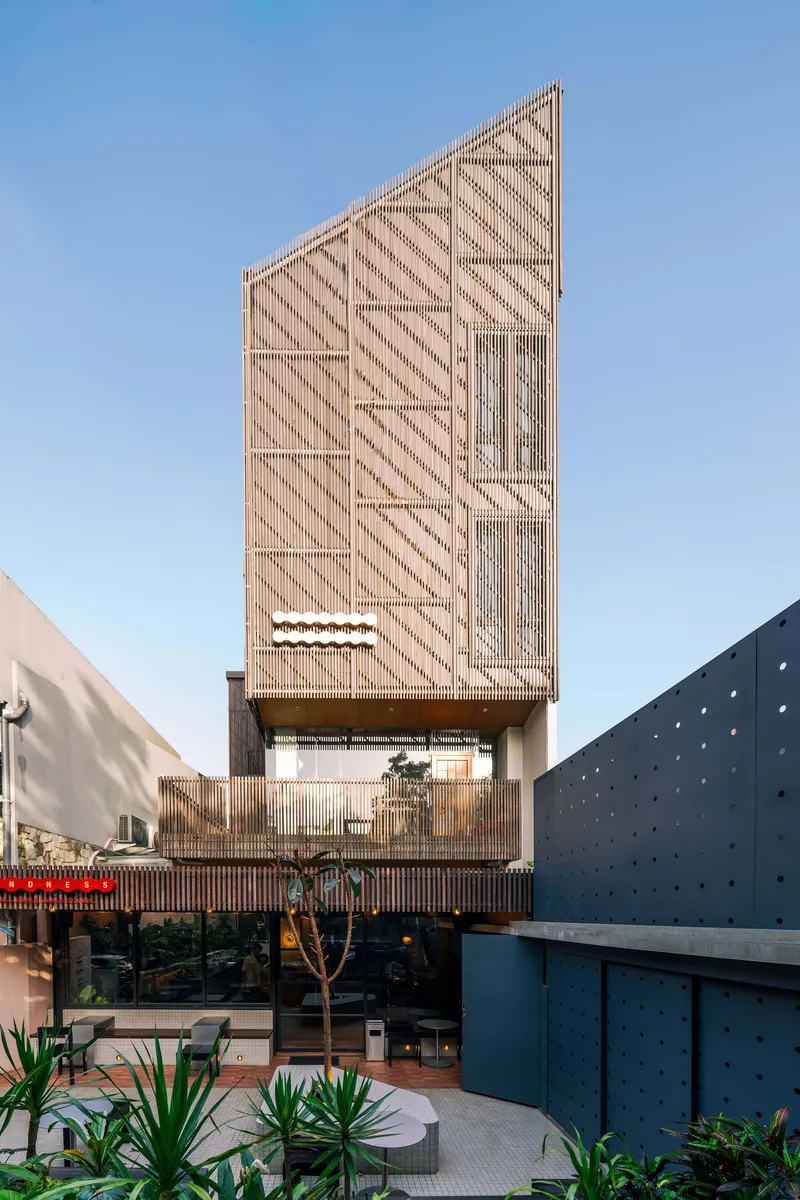 Timber-screened facade with diagonal slat patterns rising above a planted courtyard in afternoon light