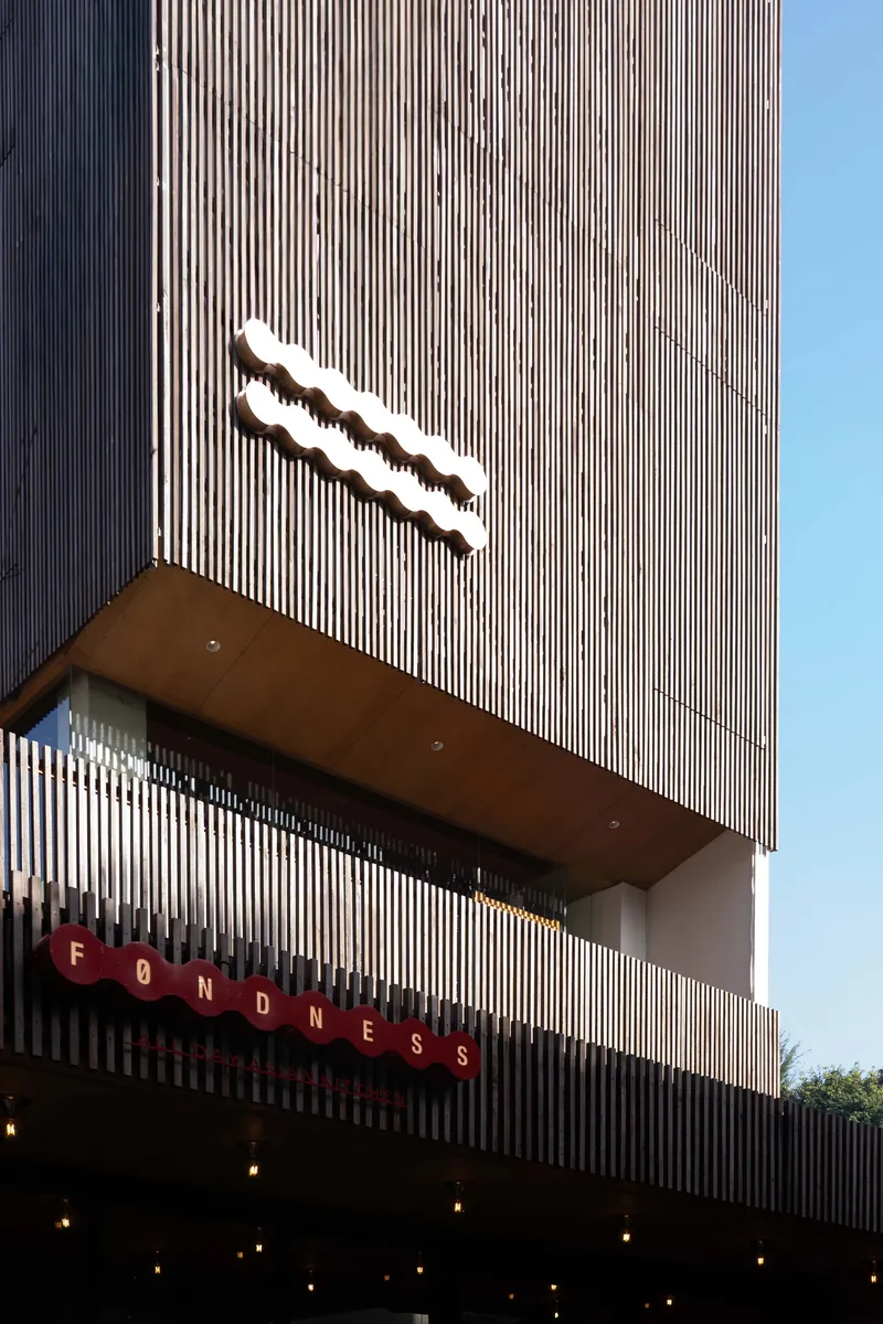 Vertically ribbed facade with a projecting canopy and illuminated signage against a clear blue sky