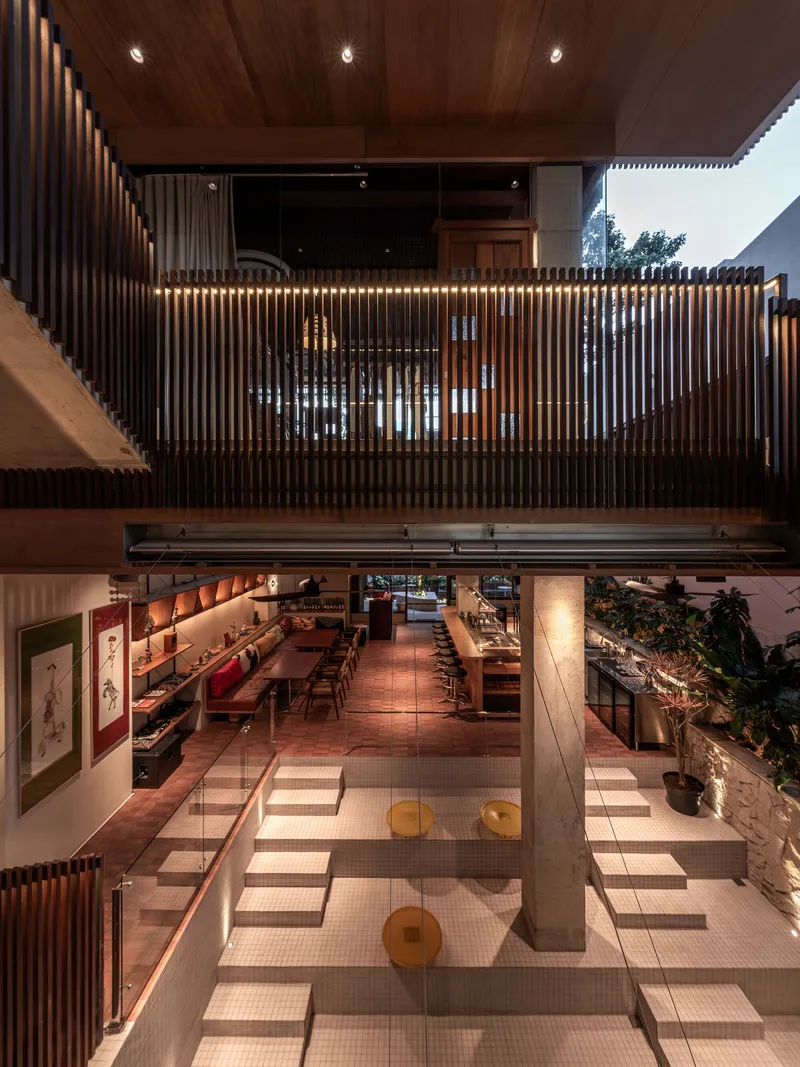 Double-height interior space with a timber slatted balustrade overlooking a tiled dining level below