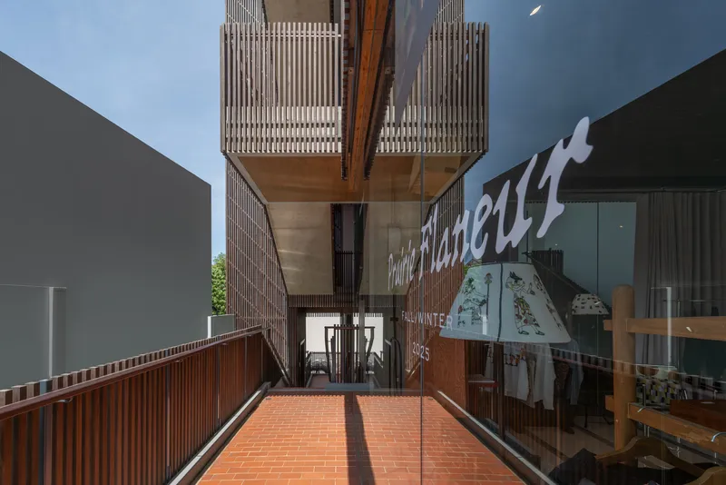 Terrace with red brick paving and timber screen walls beneath cantilevered volumes with vertical slatted cladding