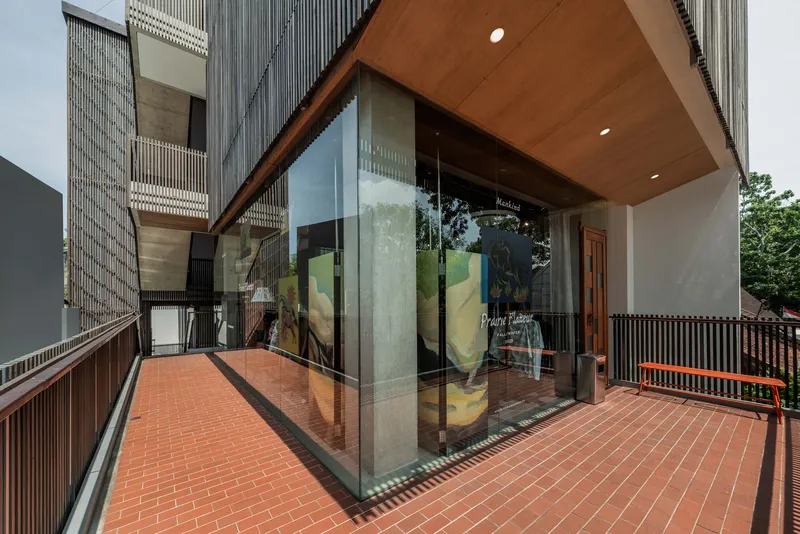 Glass-walled pavilion with timber soffit overhang opening onto a red brick terrace with perforated metal railings