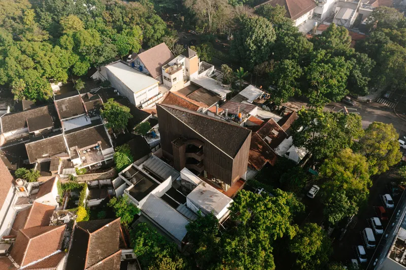 Drone view showing the vertical volume with timber cladding surrounded by low-rise residential buildings and greenery
