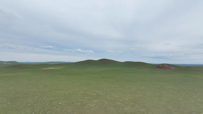 Original site photograph showing the C-shaped extinct volcano in the green grassland