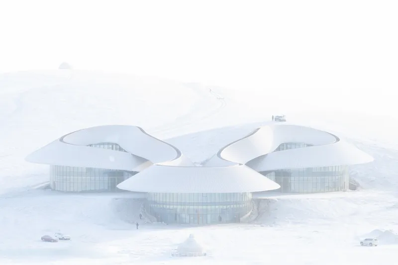 Frontal view of three lobed roof forms emerging from the snowed-over hillside