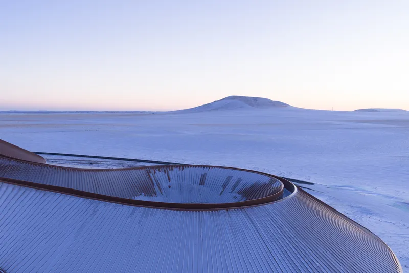 Long horizon view with the building barely visible against the snowfield at twilight