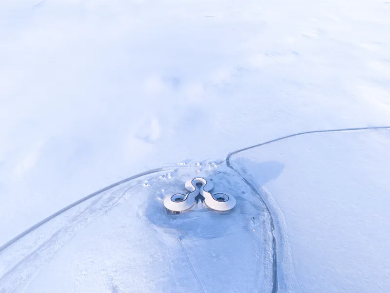 Top-down aerial showing the building as a tiny mark on the vast snowfield