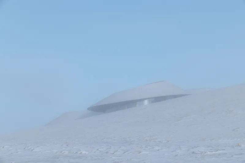 Single curved roof poking out of the snow under a clear blue sky