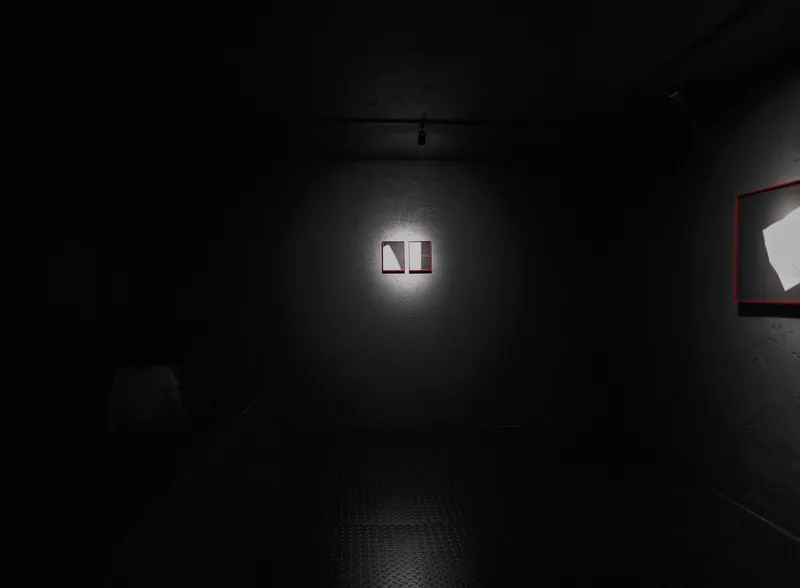 Darkened exhibition space with spotlit framed work mounted on a textured black wall