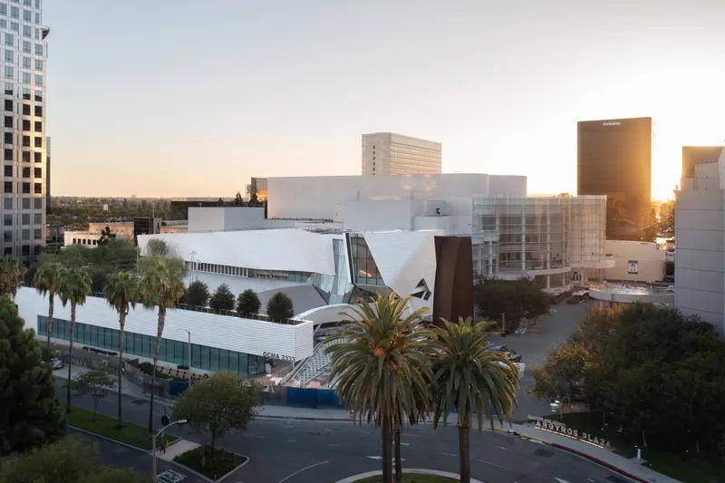 Elevated view of the white angular museum complex among palm trees at golden hour