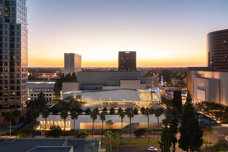 The illuminated translucent facade behind a landscaped plaza with palms at dusk