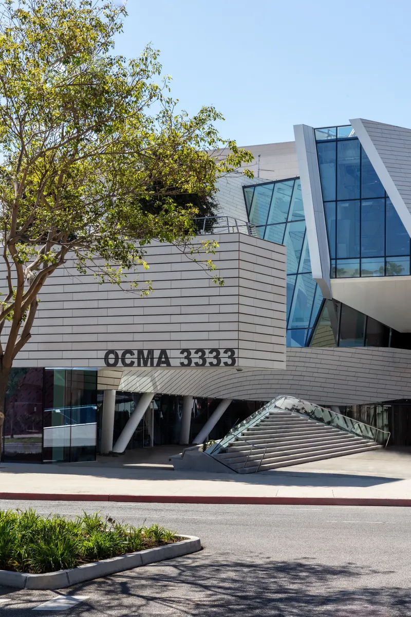 Street-level view of the horizontal cladding and angled glass entry beneath a tree
