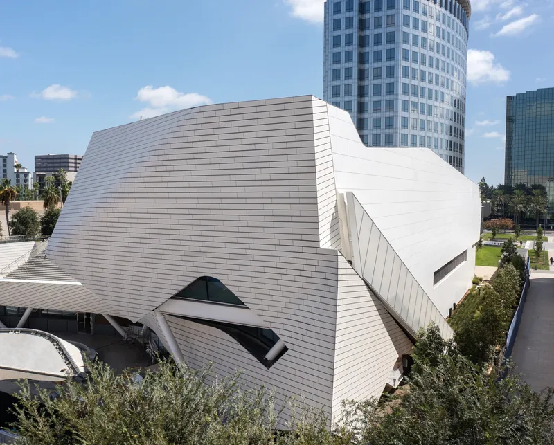 Aerial view of the ribbed white roof volumes curving past surrounding high-rise towers