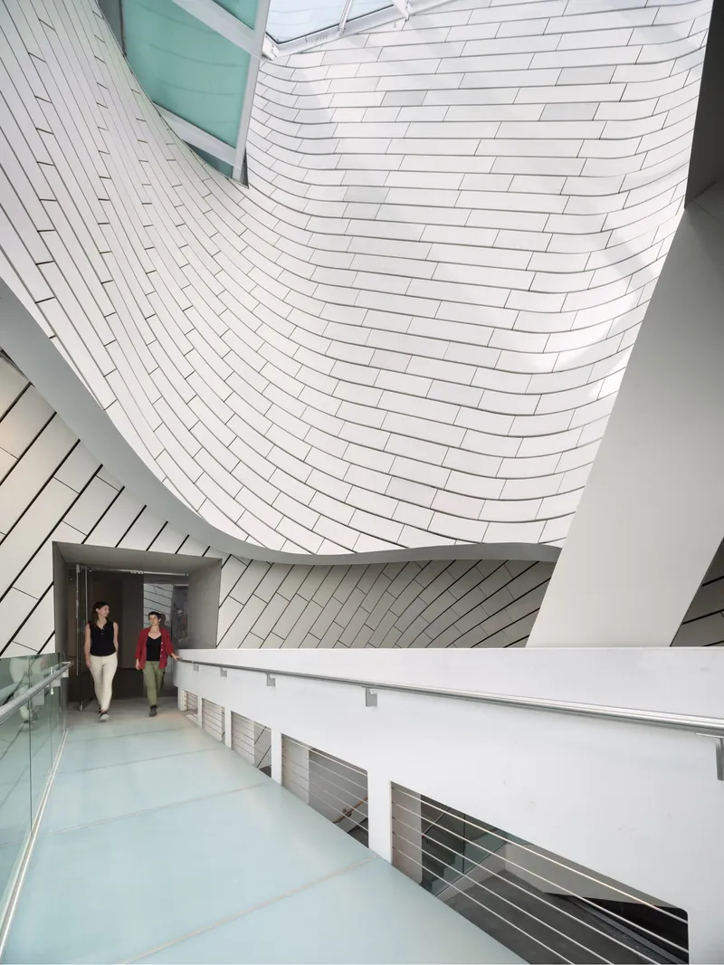 Interior ramp ascending alongside the curved white tile-clad wall with two visitors walking