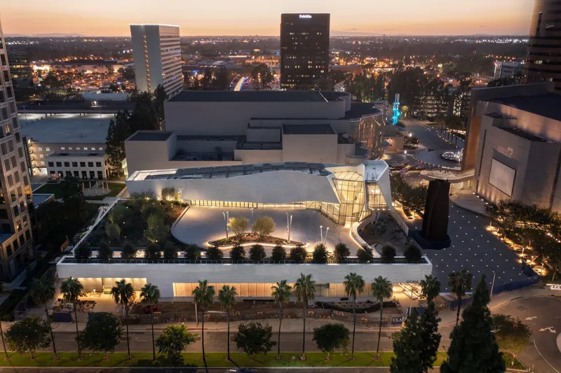 Aerial view at dusk showing the illuminated rooftop courtyard with palm trees and surrounding urban towers