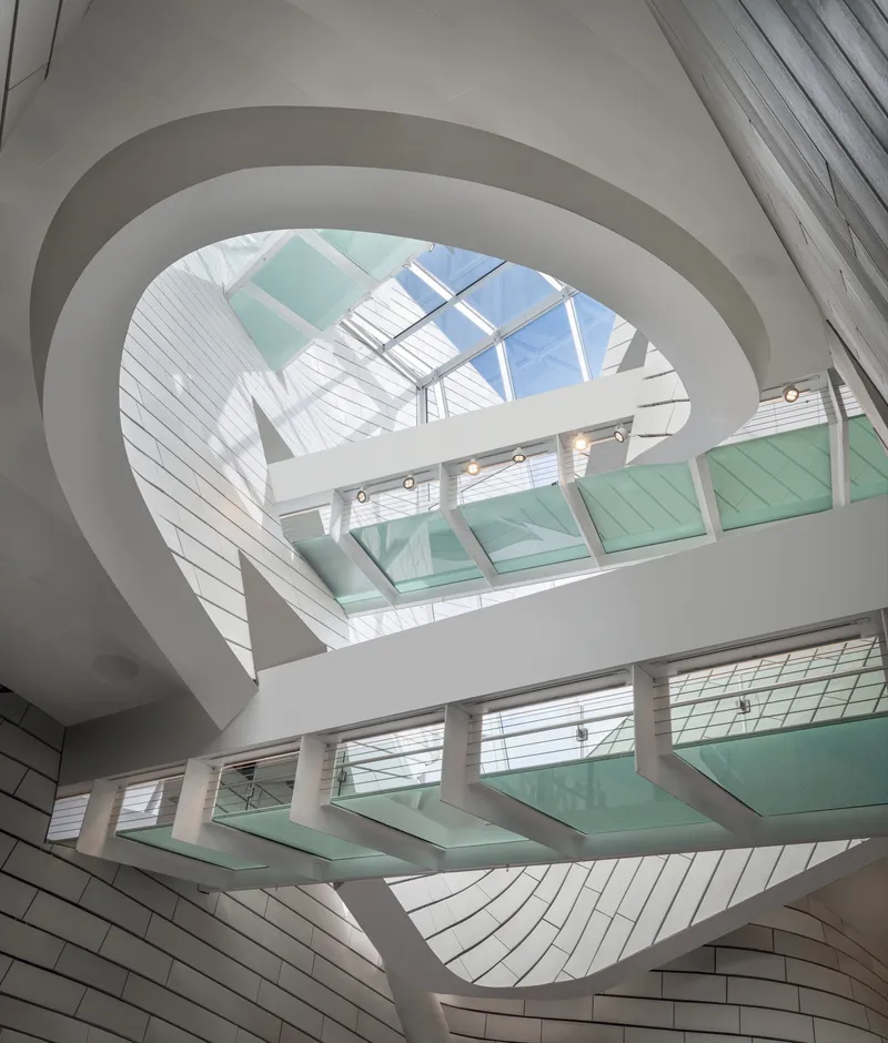 Interior atrium with spiraling white balconies, glass bridges, and skylight flooding the space with daylight