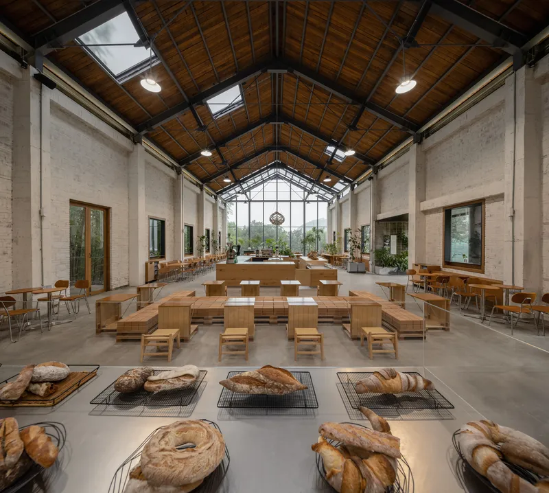Interior hall with exposed timber-planked ceiling, steel trusses, and rows of baked bread in foreground