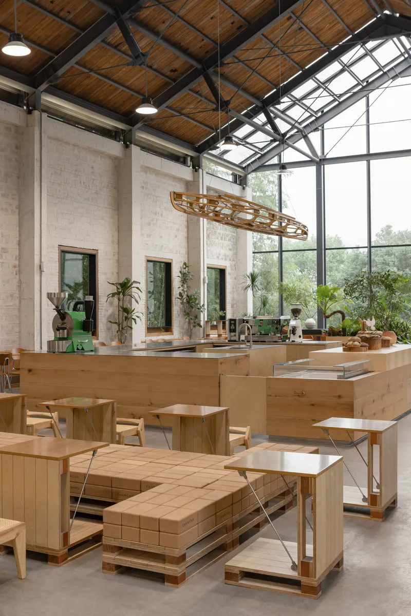 Dining hall with glazed gable end, timber service counter and sculptural pendant light suspended from exposed trusses